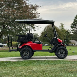 Red golf cart on a grassy area with trees and houses in the background | RM Cart 